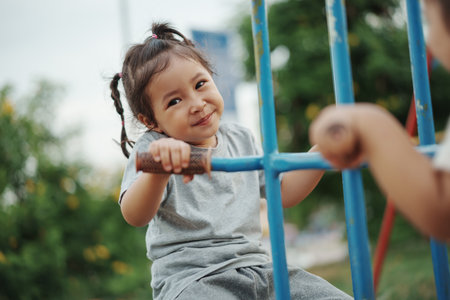 cheerful toddler girl playing on a double swing with freind at outdoor playgroundの写真素材