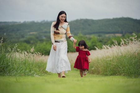 happy mother walking with her toddler girl on a grass fieldの写真素材