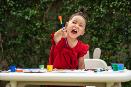 happy toddler girl painting watercolor in a paper at backyard.の写真素材