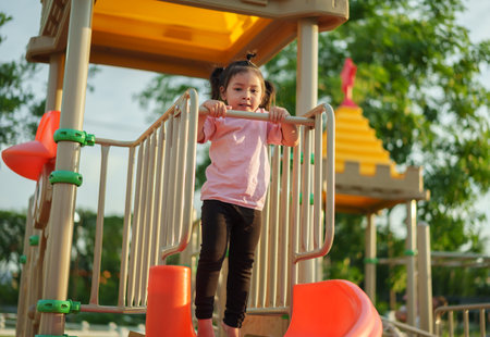 happy toddler girl hanging the bar by her hand at outdoor playground in the parkの写真素材