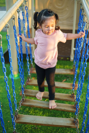 happy toddler girl playing and walking on wooden rope bridge at a outdoor playground in the parkの写真素材