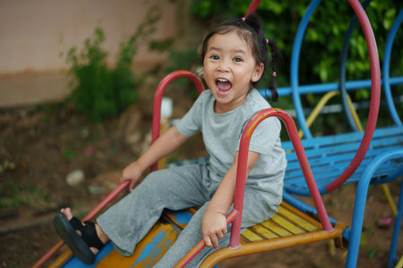 happy toddler baby girl sliding and playing at outdoor playgroundの写真素材