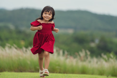 happy toddle girl in red dress running on a grass fieldの写真素材