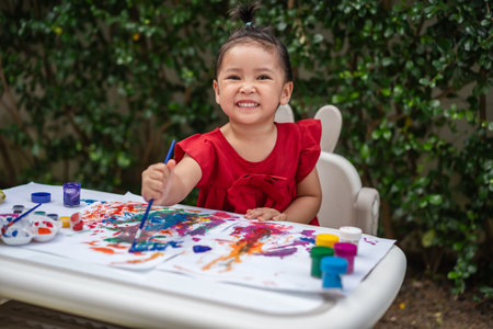 happy toddler girl painting watercolor in a paper at backyard.の写真素材