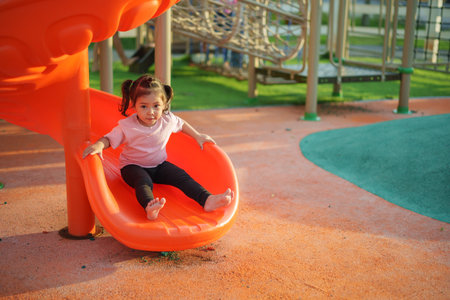 happy toddler baby girl sliding and playing at outdoor playgroundの写真素材