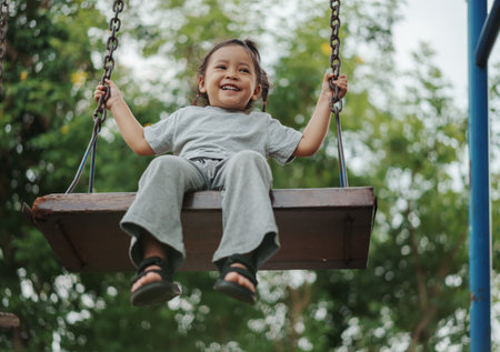 cheerful toddler girl playing on a wooden swing at playgroundの写真素材