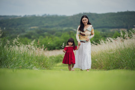 happy mother walking with her toddler girl on a grass fieldの写真素材