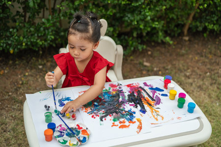 happy toddler girl painting watercolor in a paper at backyard.の写真素材