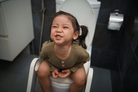 toddler girl sitting on the toilet at home and suffering from stomachache and constipationの写真素材