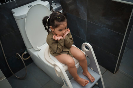 toddler girl sitting on the toilet at home and suffering from stomachache and constipationの写真素材