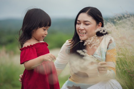happy mother and daughter playing grass flower in a fieldの写真素材