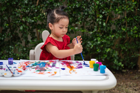 happy toddler girl painting watercolor in a paper at backyard.の写真素材