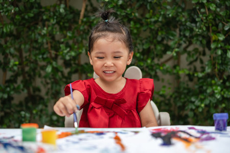 happy toddler girl painting watercolor in a paper at backyard.の写真素材