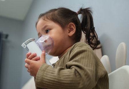 toddler girl making inhalation treatment with nebulizer in bedroom at homeの写真素材