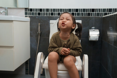 toddler girl sitting on the toilet at home and suffering from stomachache and constipationの写真素材