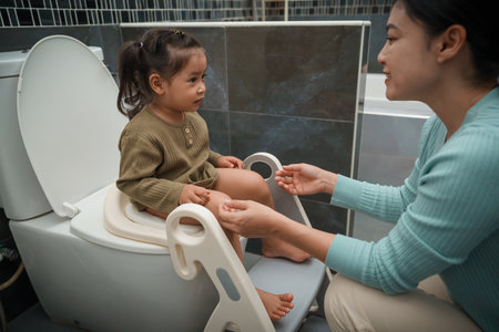 mother is helping toddler girl use the toilet. potty training and learning in the bathroomの写真素材