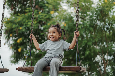 cheerful toddler girl playing on a wooden swing at playgroundの写真素材