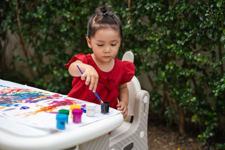 happy toddler girl painting watercolor in a paper at backyard.