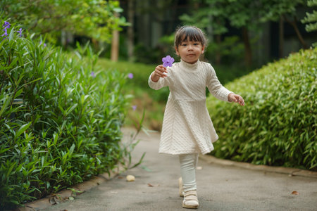 happy toddler girl in white dress with Ruellia simplex or Mexican petunia flower in the gardenの写真素材