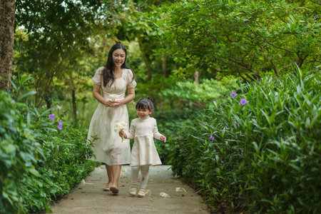 happy mother and toddler girl in white dress walking in the flower garden