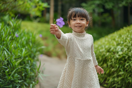happy toddler girl in white dress with Ruellia simplex or Mexican petunia flower in the gardenの写真素材