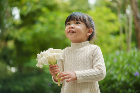 happy toddler girl in white dress with dolichandrone serrulata flower in the gardenの写真素材