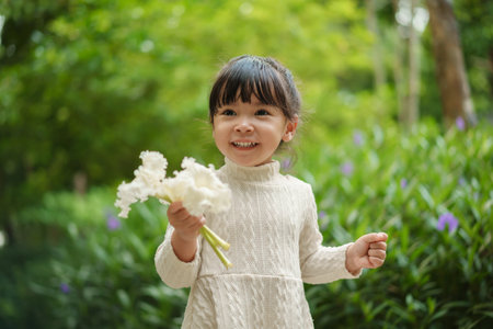 happy toddler girl in white dress with dolichandrone serrulata flower in the gardenの写真素材