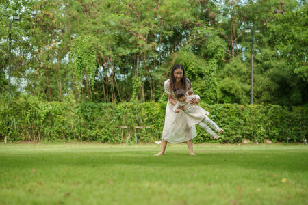 mother and toddler girl playing circling around on grass field at the parkの写真素材