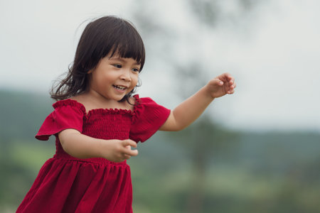 cheerful toddler girl in red dress playing in a grass fieldの写真素材