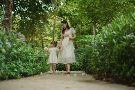 happy mother and toddler girl in white dress walking in the flower gardenの写真素材
