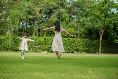 mother and toddler girl playing walk and run circling around on grass field at the parkの写真素材