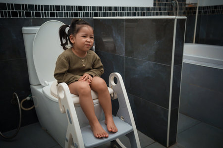 toddler girl sitting on the toilet at home and suffering from stomachache and constipationの写真素材