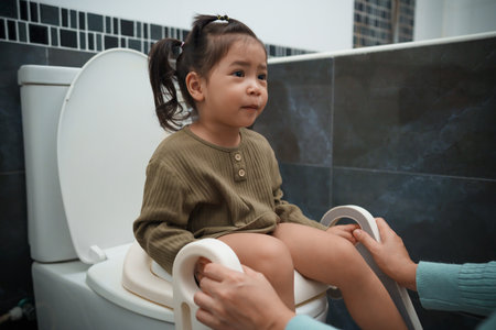 mother is helping toddler girl use the toilet. potty training and learning in the bathroomの写真素材