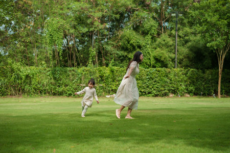 mother and toddler girl playing walk and run circling around on grass field at the parkの写真素材