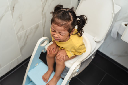toddler girl sitting on a toilet at home and suffering from stomachache and constipation