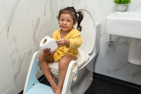 happy toddler girl is sitting on the toilet with tissue at home. potty training and learningの写真素材