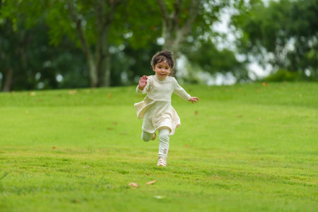 happy toddler girl in white dress running on a green grass fieldの写真素材