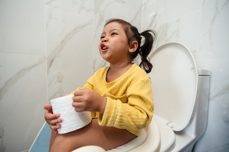 toddler girl sitting on a toilet with tissue at home