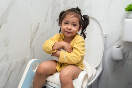happy toddler girl is sitting on the toilet with tissue at home. potty training and learningの写真素材
