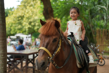happy toddler girl riding brown horse in parkの写真素材