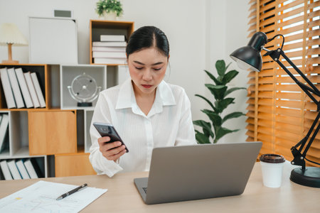 stressed young woman working with smartphone and laptop computer at home officeの写真素材