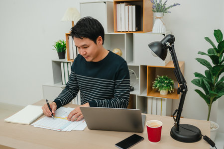 happy man writing document or paperwork with a laptop at home office
