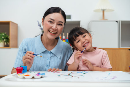 happy mother and toddler girl painting watercolor in a paper at homeの写真素材