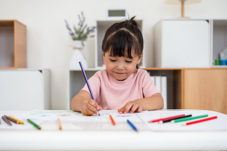 happy toddler baby girl training to drawing with colored pencil on a desk at homeの写真素材