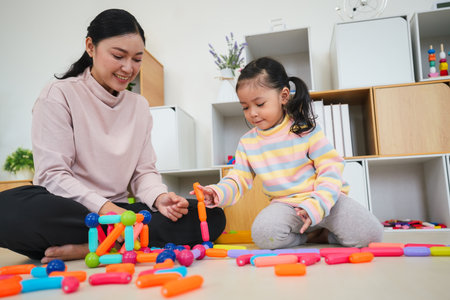 happy toddler girl and mother playing colorful magnetic construction toy at homeの写真素材