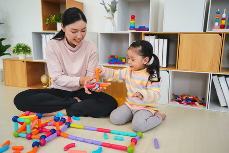 happy toddler girl and mother playing colorful magnetic construction toy at homeの写真素材