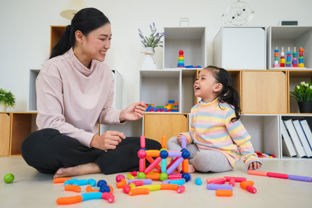 happy toddler girl and mother playing colorful magnetic construction toy at homeの写真素材