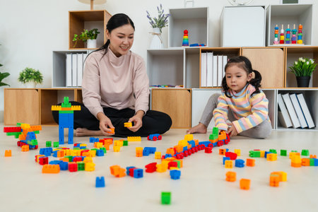 happy toddler girl and her mother playing building blocks or plastic bricks toy at homeの写真素材
