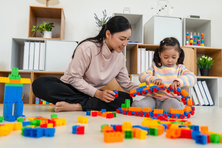 happy toddler girl and her mother playing building blocks or plastic bricks toy at homeの写真素材