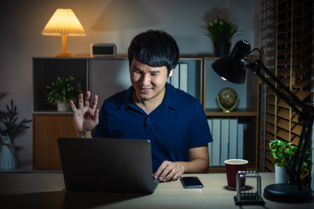 happy man using laptop and wireless earbuds making video call at a nightの写真素材